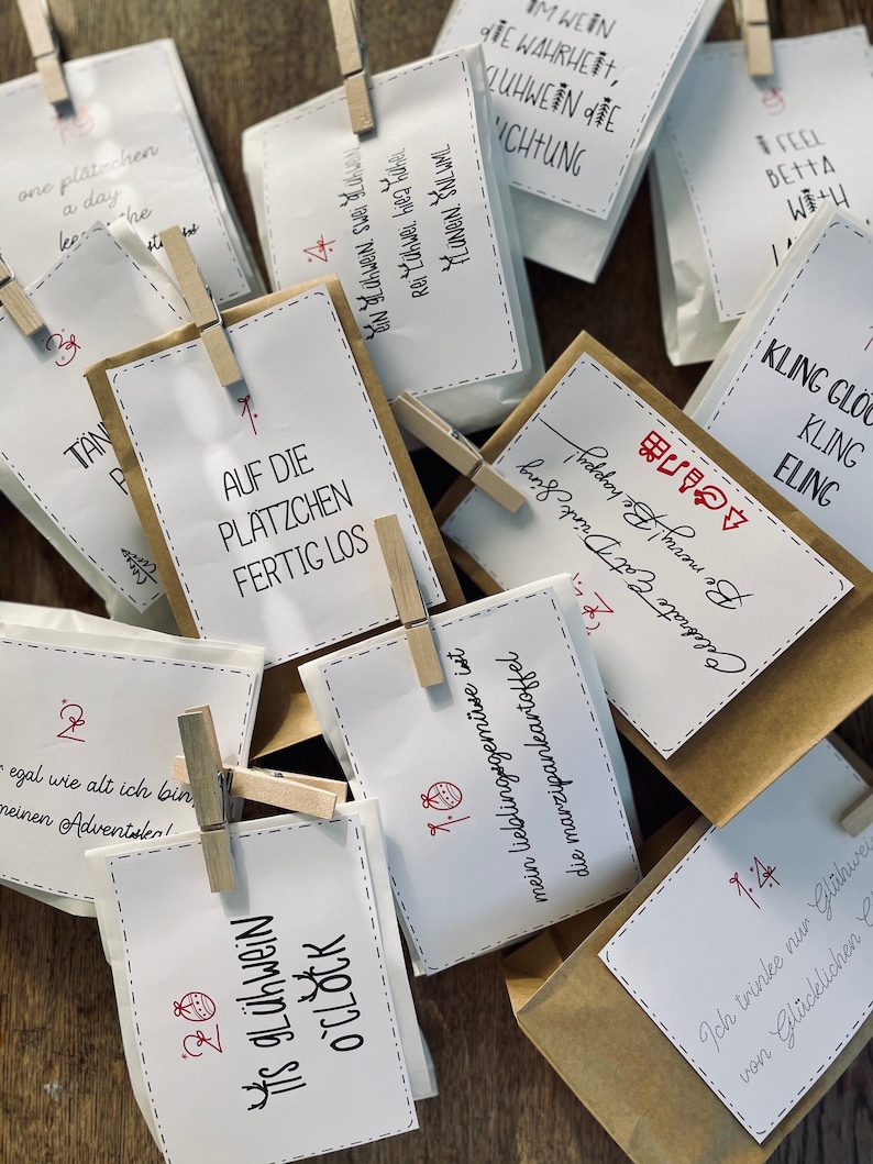 K&ouml;nnte beinhalten: Eine Sammlung kleiner brauner Papiert&uuml;ten mit wei&szlig;en Papieretiketten. Die Etiketten tragen verschiedene Weihnachtsbotschaften, die in Schwarz und Rot geschrieben sind. Einige der Botschaften lauten "Is gl&uuml;hwein o'clock", "Auf die Pl&auml;tzchen fertig los" und "Ich trinke nur Gl&uuml;hwein von Gl&uuml;cklichen".