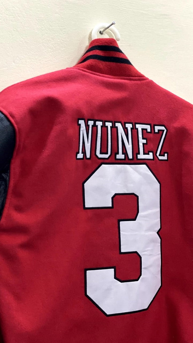 May include: Red varsity jacket with black leather sleeves. The back of the jacket has white lettering that says "NUNEZ" and the number "3" in white with a black outline.