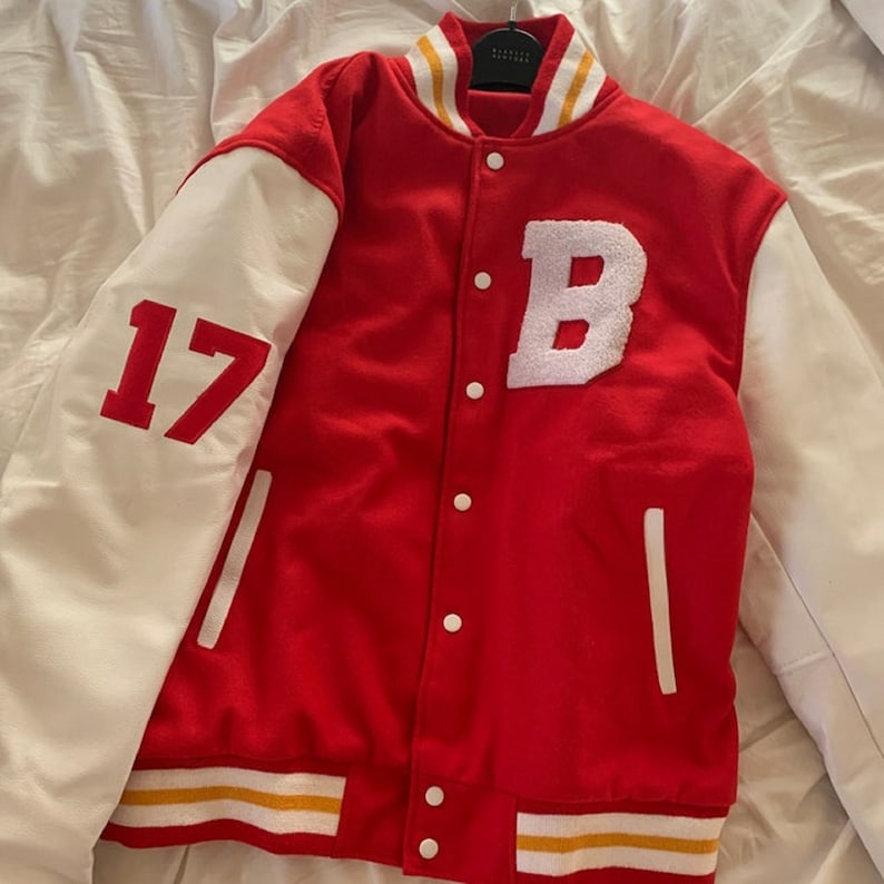 May include: Red and white varsity jacket with a white letter "B" on the front and the number "17" on the left sleeve. The jacket has a gold and white striped trim around the bottom and collar.