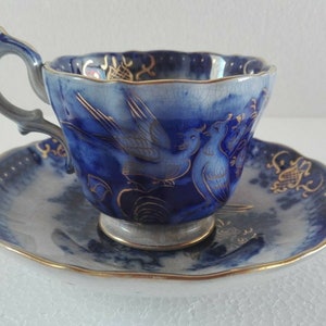 Pode incluir: Um conjunto de chávena e pires azul e dourado com um design de pássaro. A chávena e o pires são decorados com detalhes dourados e um padrão floral azul e branco.
