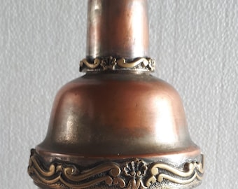 May include: A copper and silver decorative bottle with an ornate brass trim. The bottle has a round body and a narrow neck.