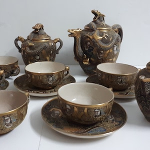 Pode incluir: Um conjunto de chá japonês em ouro e preto com desenhos de dragões e flores. O conjunto inclui uma chaleira, um jarro de creme, um açucareiro e seis xícaras de chá e pires.