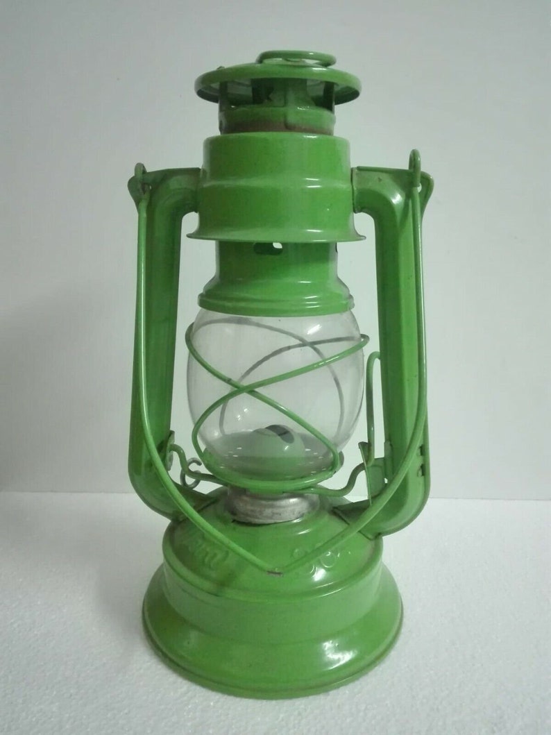 以下が含まれることがあります： 透明なガラスのグローブとワイヤーケージが付いた緑色の金属製のケロシンランタン。ランタンは両側にハンドルがあり、丸いベースがあります。
