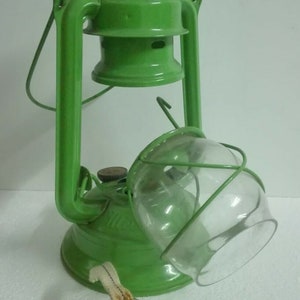 以下が含まれることがあります： ガラスのグローブと金属製の芯ホルダーが付いた緑色の灯油ランタン。ランタンには持ち運び用のハンドルと金属製の蓋が付いています。