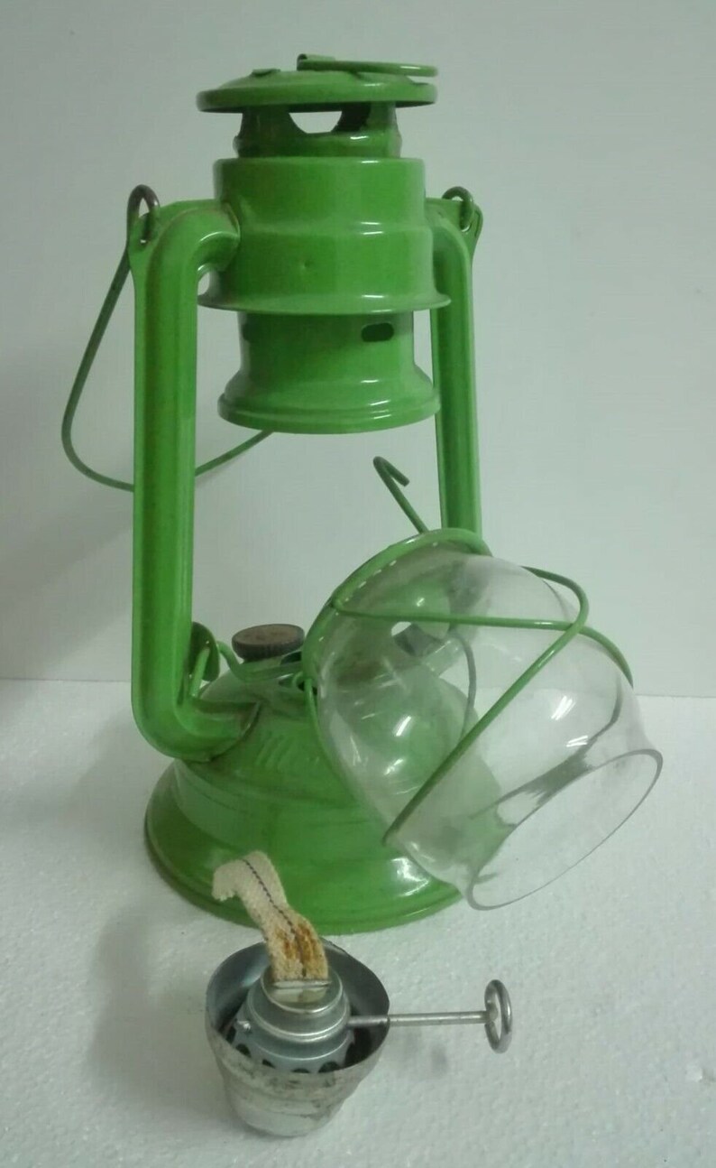 以下が含まれることがあります： ガラスのグローブと金属製の芯ホルダーが付いた緑色の灯油ランタン。ランタンには持ち運び用のハンドルと金属製の蓋が付いています。