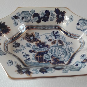Pode incluir: Prato de servir octogonal em porcelana com um design floral em tons de azul e branco. O prato tem uma borda dourada e um padrão detalhado de flores e folhagens. Uma peça decorativa para servir alimentos.