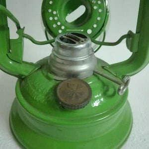 以下が含まれることがあります： 緑色の金属製のケロシンランタン。銀色のバーナーと丸い緑色の金属製のキャップが付いています。ランタンは透明なガラスのグローブと金属製のハンドルが付いています。