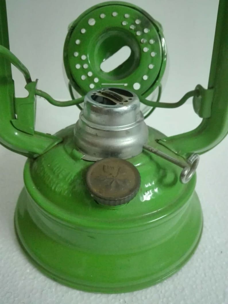 以下が含まれることがあります： 緑色の金属製のケロシンランタン。銀色のバーナーと丸い緑色の金属製のキャップが付いています。ランタンは透明なガラスのグローブと金属製のハンドルが付いています。