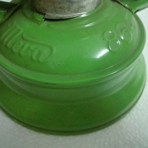 以下が含まれることがあります： 銀色のトップと側面に「Mera」という文字が刻印された緑色の金属製のケロシンランプです。