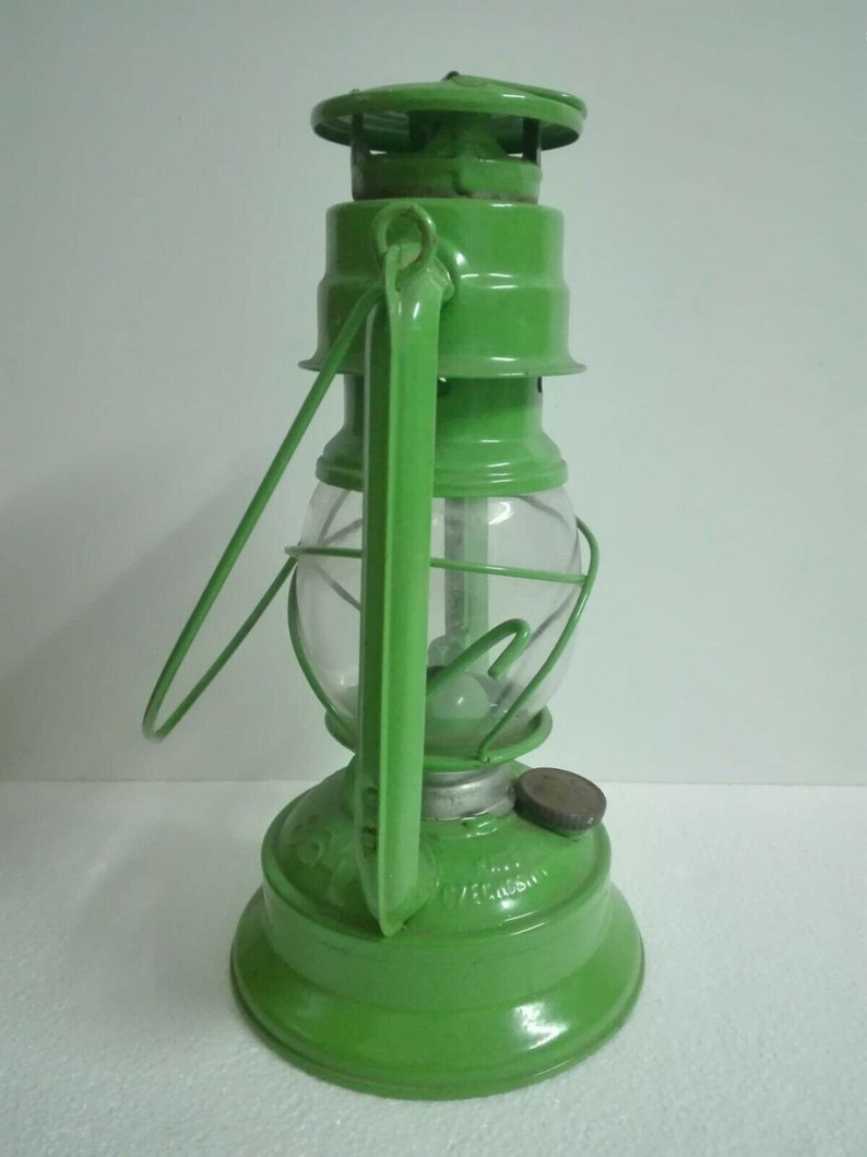 以下が含まれることがあります： 透明なガラスのグローブとワイヤーケージが付いた緑色の金属製のケロシンランタン。ランタンにはハンドルと金属製のキャップが付いています。
