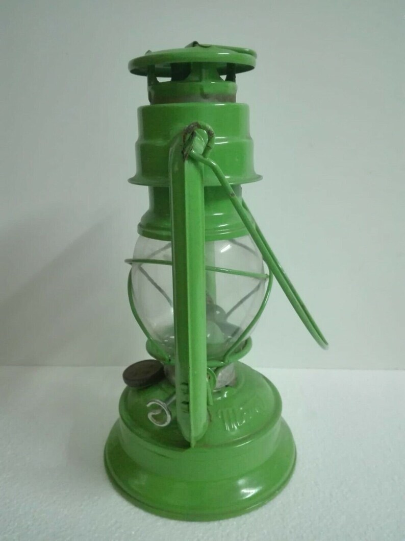 以下が含まれることがあります： ガラスのグローブとワイヤーケージが付いた緑色の金属製のケロシンランタン。ランタンにはハンドルと金属製のキャップが付いています。