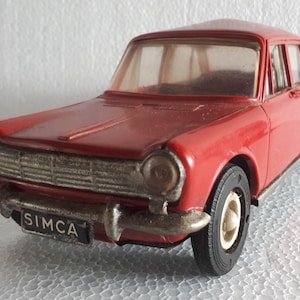 Può includere: Un'auto giocattolo rossa modello Simca 1000, un'auto francese classica. L'auto ha una griglia anteriore dettagliata, fari e un parabrezza. L'auto ha la scritta "SIMCA" stampata sul paraurti anteriore.