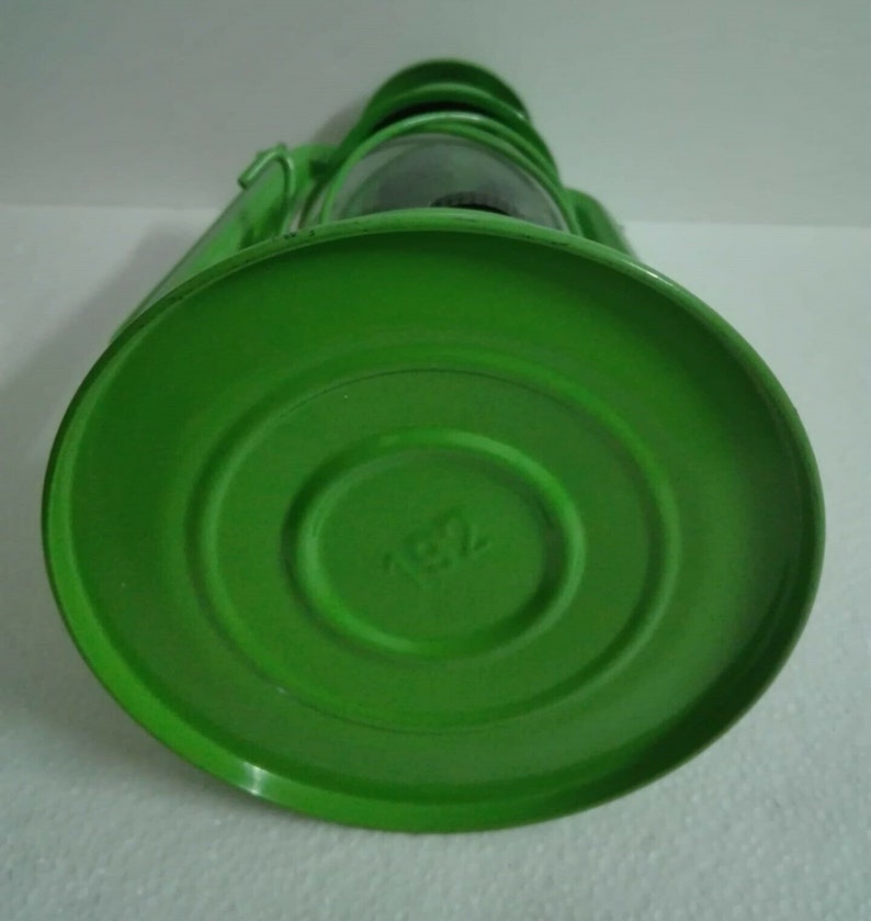 以下が含まれることがあります： ガラスのグローブと円形のベースが付いた緑色の金属製のランタン。ベースには小さなエンボス加工のデザインが施されています。