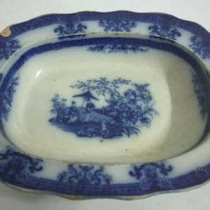 May include: A blue and white oval serving dish with a scalloped edge. The dish features a transferware design of a Chinese scene with figures and trees.