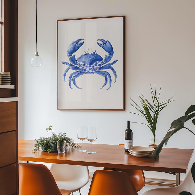 May include: A framed art print featuring a detailed blue crab illustration. The crab is depicted in a watercolor style, set against a white background, and framed in a warm brown wood. The artwork is displayed in a dining room setting.