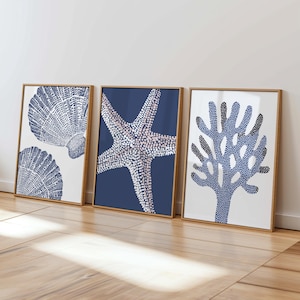 Puede incluir: Tres impresiones artísticas enmarcadas con motivos marinos. Las impresiones muestran una concha, una estrella de mar y un diseño de coral, todos en tonos azules y blancos sobre un fondo neutro. Los marcos son de madera natural.