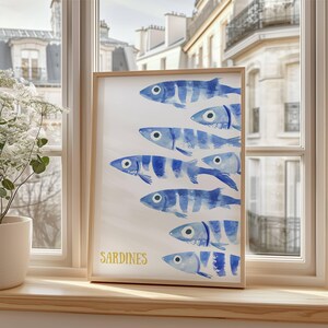 K&ouml;nnte beinhalten: Ein gerahmter Aquarelldruck einer Schule von blauen und wei&szlig;en Sardinen, die in einer Reihe schwimmen. Der Druck hat das Wort "SARDINEN" in Gelb unten geschrieben.