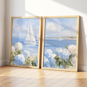 May include: Two framed landscape paintings. Each features a coastal scene with sailboats on blue water, white clouds, and blue and white hydrangea flowers. The frames are light wood.