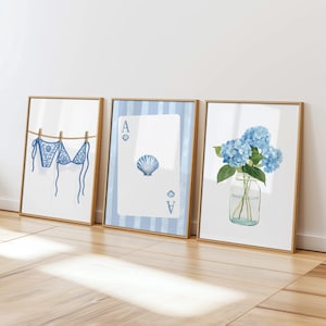 May include: Three framed art prints with a beach theme. One print shows a blue bikini hanging on a clothesline. Another features a playing card with a seashell. The third displays blue hydrangeas in a glass jar. All are in gold frames.