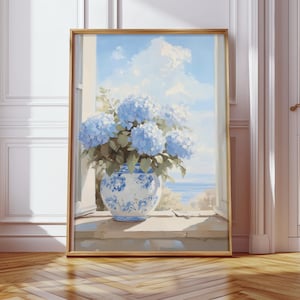 Op de afbeelding: Een ingelijst schilderij van een blauw-witte vaas gevuld met blauwe hortensia's. De vaas staat op een vensterbank met uitzicht op een zeegezicht met een blauwe lucht en witte wolken. De lijst is goudkleurig.