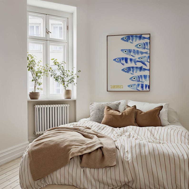 K&ouml;nnte beinhalten: Ein wei&szlig;-braunes gestreiftes Bett mit einer braunen Decke und ein paar Kissen. &Uuml;ber dem Bett h&auml;ngt ein blaues und wei&szlig;es Aquarellbild von Sardinen. Das Bild tr&auml;gt unten den Schriftzug "SARDINES" in Gelb.