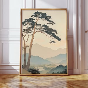 May include: A framed art print depicting a Japanese-style landscape. It features a pine tree with dark green foliage and a light brown trunk. The background shows a mountain range in shades of blue and beige, with a river and forest in the foreground.