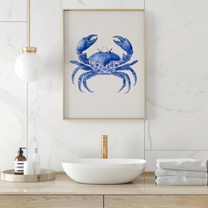 May include: A framed art print featuring a blue crab illustration. The crab is depicted in a detailed watercolor style, with a decorative pattern on its shell. The artwork is set against a neutral background, framed in gold, and suitable for coastal decor.