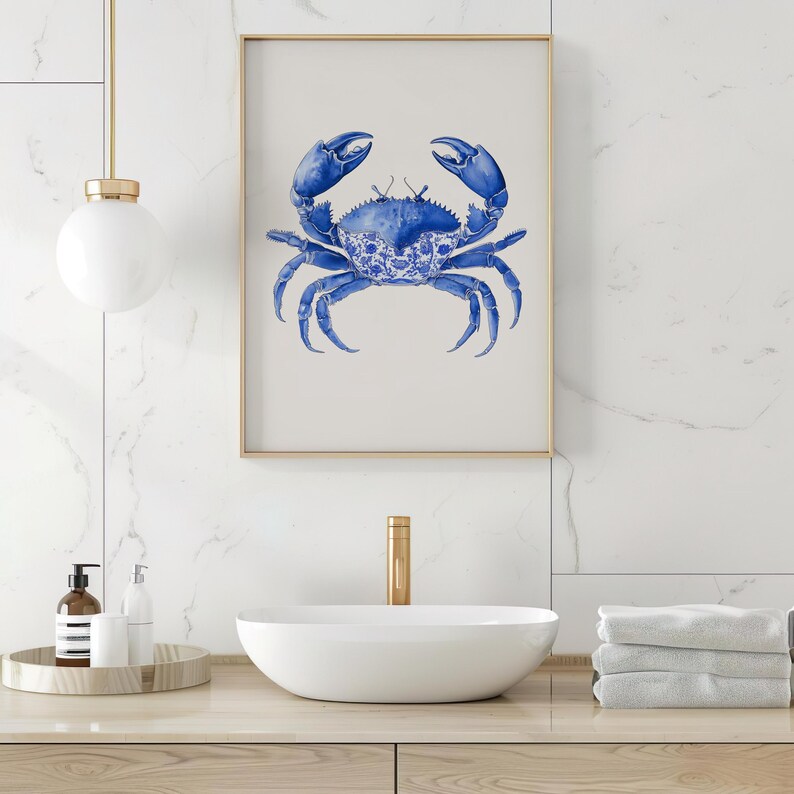 May include: A framed art print featuring a blue crab illustration. The crab is depicted in a detailed watercolor style, with a decorative pattern on its shell. The artwork is set against a neutral background, framed in gold, and suitable for coastal decor.