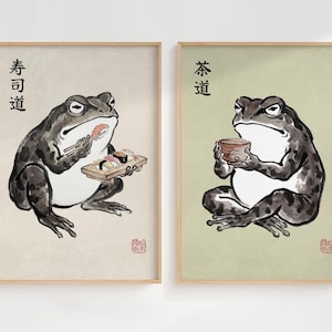 Könnte beinhalten: Zwei gerahmte Kunstdrucke. Einer zeigt einen Frosch mit Sushi, der andere einen Frosch mit einer Teetasse. Japanischer Text befindet sich über jedem Frosch. Der Kunststil erinnert an traditionelle japanische Tuschemalerei.
