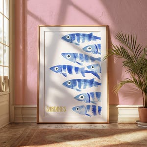 K&ouml;nnte beinhalten: Ein gerahmter Aquarelldruck einer Schule von blau-wei&szlig; gestreiften Sardinen, die in einer Reihe schwimmen. Das Wort "SARDINEN" ist in goldenen Buchstaben am unteren Rand des Drucks geschrieben.