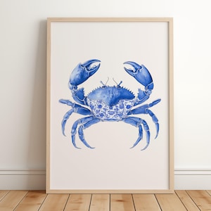 May include: A framed watercolor print of a blue crab. The crab has a detailed design on its shell, with a blue and white floral pattern. The crab's claws are raised, and the artwork is set against a white background.