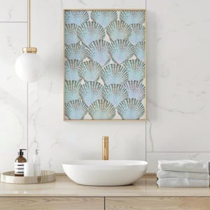 Op de afbeelding: Een ingelijste wandkunstprint met een patroon van lichtblauwe en iriserende schelpen. Het kunstwerk wordt getoond boven een witte ovale wastafel met een gouden kraan. De badkameromgeving omvat een houten aanrecht en een marmerpatroonmuur.