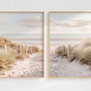May include: A set of two vertical wall art prints featuring a sandy beach path lined with tall dune grass and wooden posts. The scene depicts a light-colored wooden boardwalk leading toward the ocean under a soft, pale sky with gentle clouds.