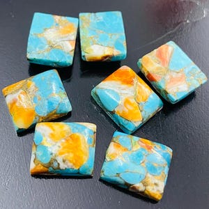 Può includere: Sette cabochon quadrati di pietre preziose turchesi con venature arancioni, bianche e dorate. Le pietre preziose sono disposte su una superficie scura, mostrando i loro colori vivaci e i motivi unici. Ideale per la creazione di gioielli.