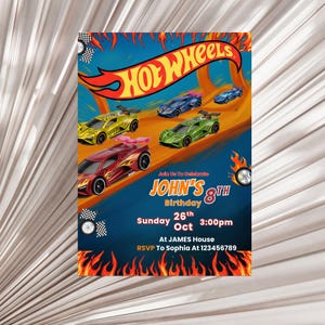 Puede incluir: Una colorida invitación de cumpleaños de Hot Wheels con coches de carreras de juguete en una pista. La invitación incluye el texto "Hot Wheels", "8º Cumpleaños de John", fecha, hora e información de RSVP. Las llamas y las banderas a cuadros decoran los bordes.