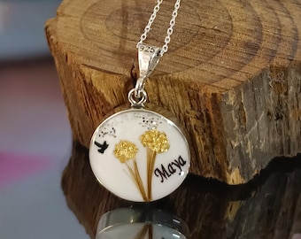 May include: A silver chain necklace with a round pendant featuring a pressed flower design and the name "Maya" inscribed on it.