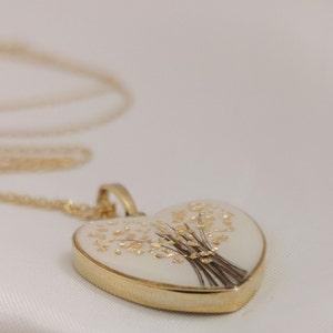 Op de afbeelding: Een gouden hartvormige ketting met een hanger in de vorm van een wit ge&euml;mailleerd hart met een gouden bloemenmotief.