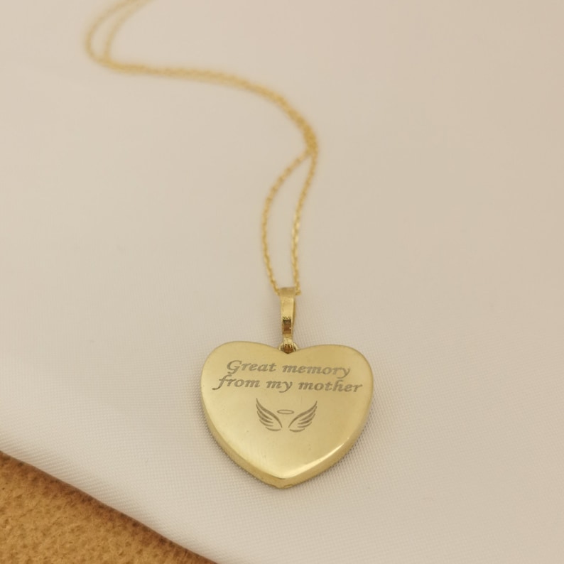 Op de afbeelding: Gouden ketting met een hartvormige hanger. De hanger heeft een inscriptie met de tekst "Great memory from my mother" met een paar engelenvleugels boven de tekst.