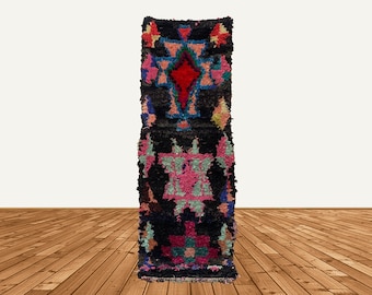 Puede incluir: Una alfombra larga y estrecha con fondo negro y coloridos patrones geométricos. La alfombra está hecha de lana y tiene una textura tejida a mano.