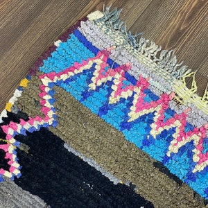 May include: A colorful, hand-woven rug with a geometric pattern in shades of blue, pink, yellow, and black. The rug has a fringe border and is made of a soft, textured material.
