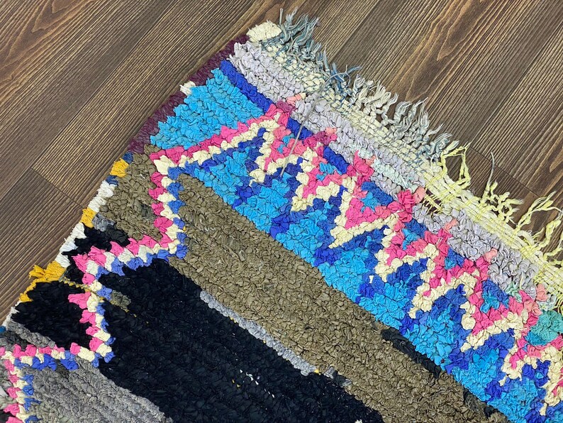 May include: A colorful, hand-woven rug with a geometric pattern in shades of blue, pink, yellow, and black. The rug has a fringe border and is made of a soft, textured material.