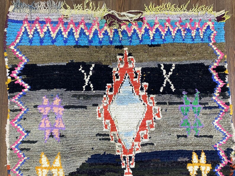May include: A colorful Moroccan rug with a diamond-shaped pattern in the center. The rug is made of wool and has a fringe border.