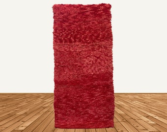 May include: A long, narrow, red rug with a fuzzy texture. The rug is made of a soft, plush material and has a subtle, woven pattern.