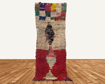 Puede incluir: Una alfombra larga y rectangular con un patrón geométrico colorido en la parte superior y un gran diseño abstracto rojo en el centro. La alfombra está hecha de un material grueso y texturizado y tiene una franja en la parte inferior.
