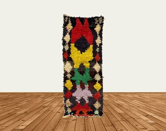 Puede incluir: Una alfombra colorida tejida a mano con un patrón geométrico en tonos de rojo, amarillo, verde y negro. La alfombra tiene un borde con flecos y está hecha de lana.
