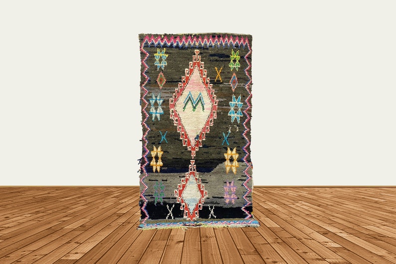 May include: A dark brown rug with a colorful diamond pattern in the center. The diamond pattern features pink, white, blue, and green colors. The rug has a fringe border.