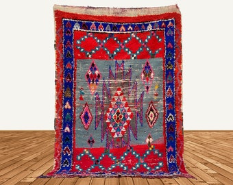 May include: A vintage Moroccan rug with a red, blue, and white geometric pattern. The rug has a faded, distressed look and is made of wool.