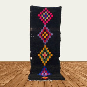 May include: A black rug with a vertical pattern of colorful diamond shapes. The rug has a fringe on the bottom.