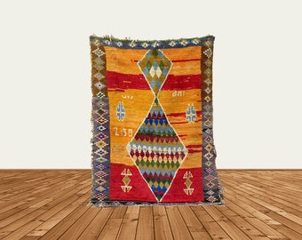 Può includere: Un tappeto marocchino colorato con un motivo a rombi in tonalità di rosso, blu, verde e giallo. Il tappeto ha un bordo con frange ed è tessuto con dettagli intricati.