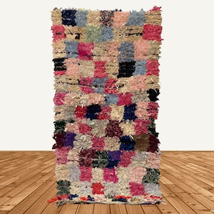 May include: A colourful Moroccan rug with a patchwork design in shades of pink, blue, green, and brown. The rug is made of wool and has a fringed edge.